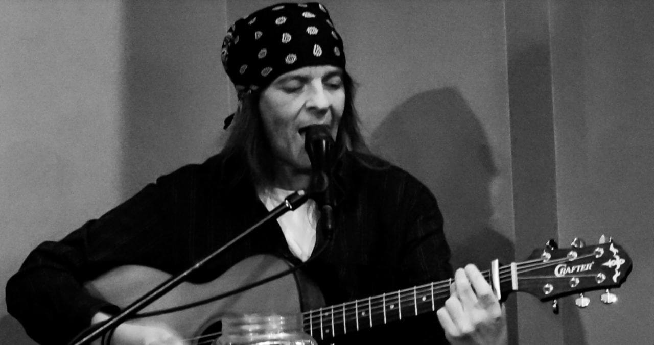A person with long hair wearing a bandana and playing a guitar
