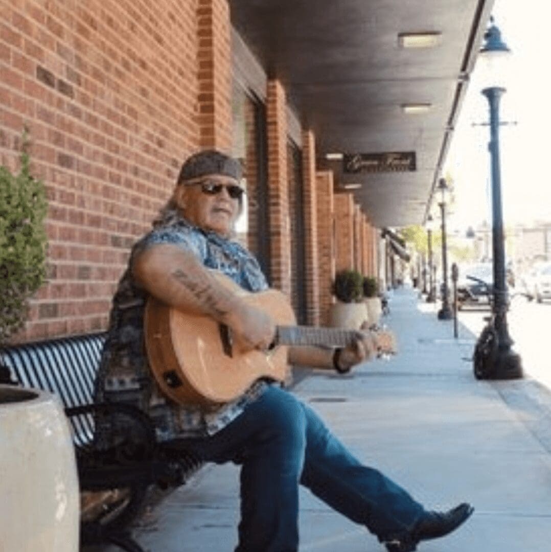 A man sitting on a bench with a guitar.