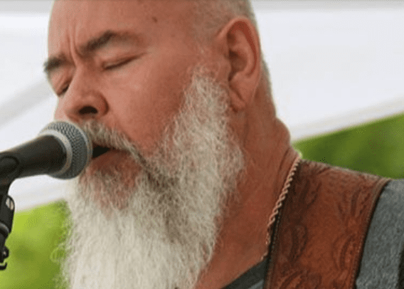 A man with a white beard singing into a microphone.