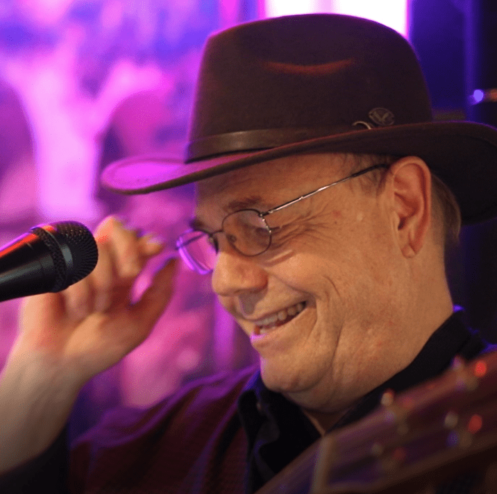 A man wearing a hat and playing an acoustic guitar.