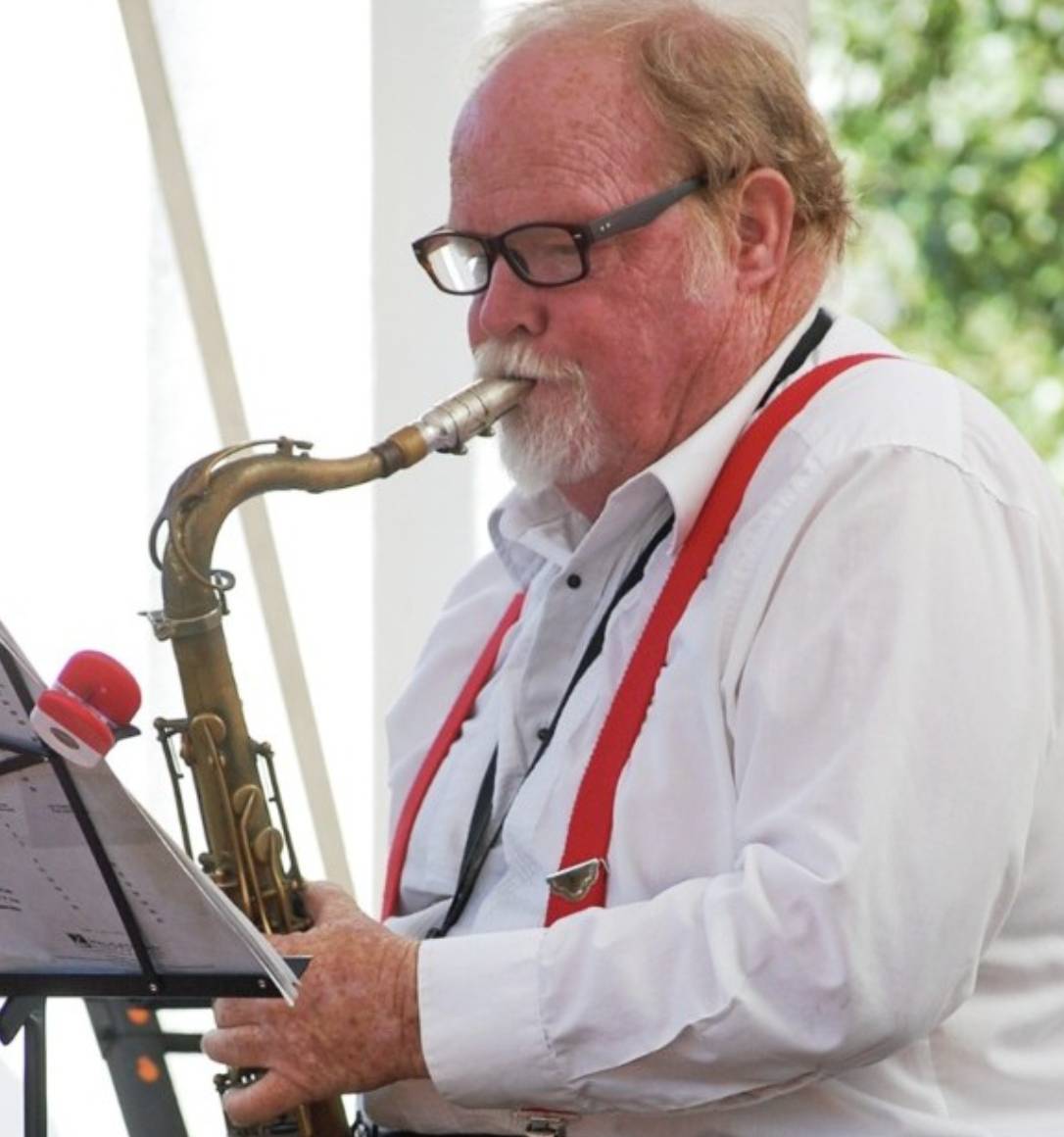 A man with glasses and suspenders playing a saxophone.