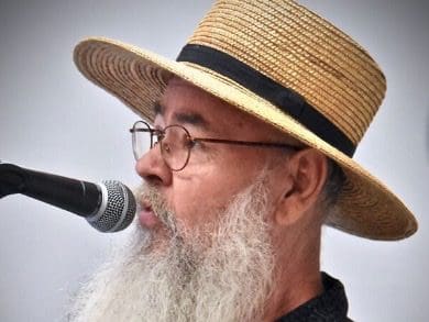 A man with a beard and glasses is singing into a microphone.