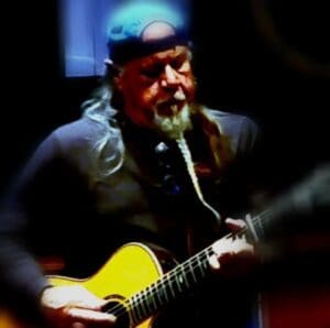 A man with a beard playing an acoustic guitar.