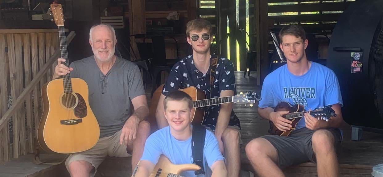 A group of people sitting on a porch with guitars and ukuleles.