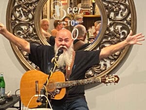 A man with a beard playing an acoustic guitar in front of a mirror.