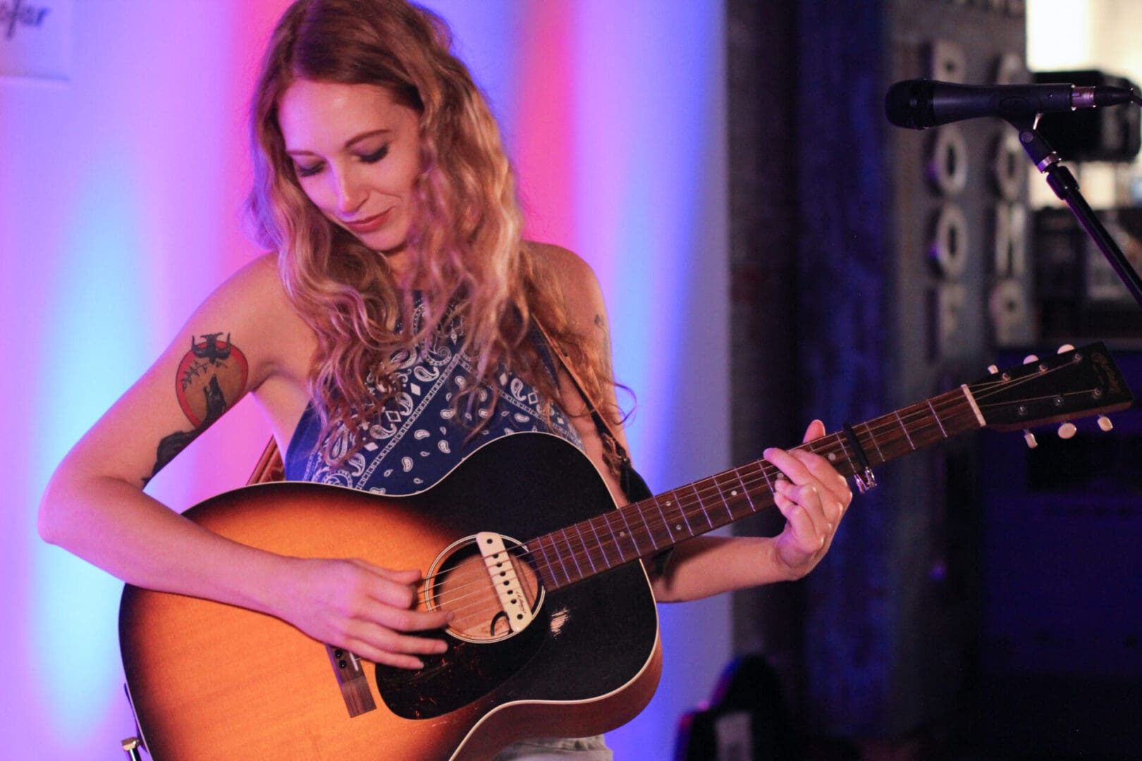 A woman playing an acoustic guitar in front of a microphone.