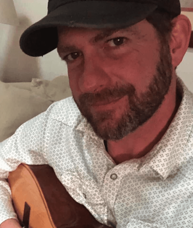 A man wearing a hat and holding an acoustic guitar.