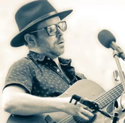 A man in a hat playing an acoustic guitar.